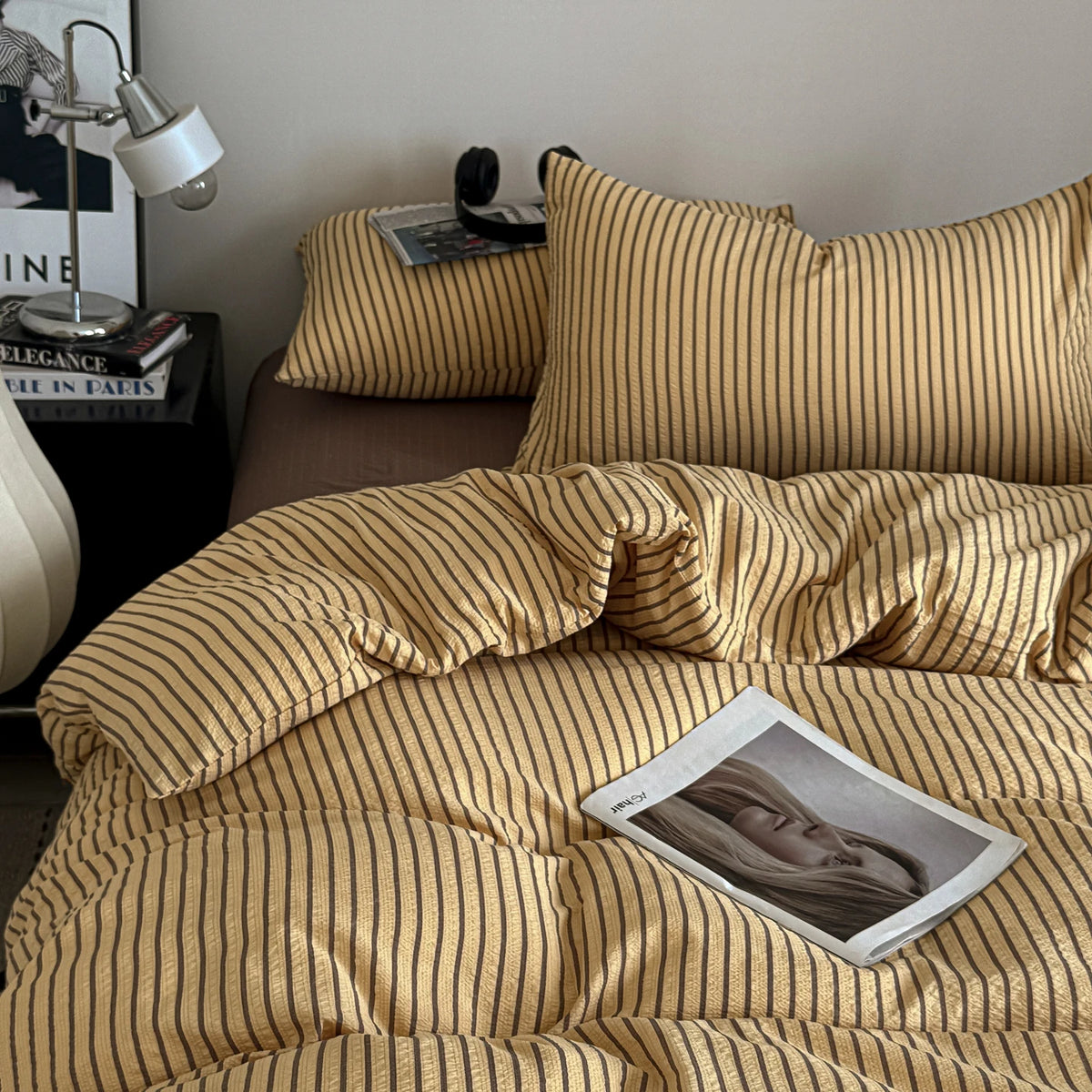 A close-up of a striped duvet cover set in gold and beige tones with a photographic print on the bed.