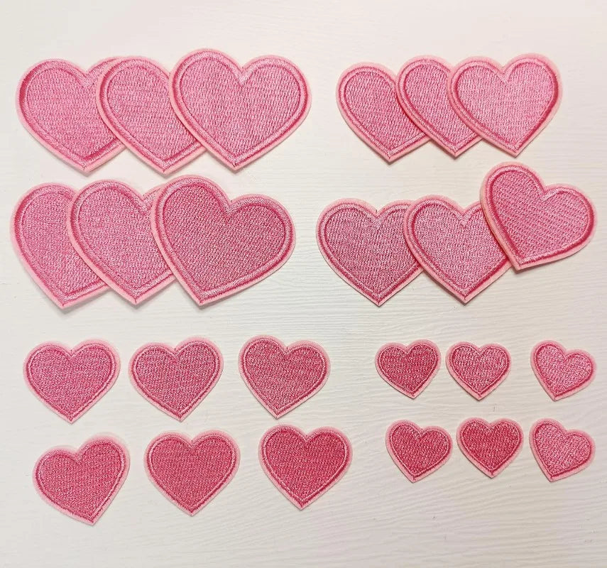 A collection of 24 pink iron-on love heart embroidered patches for DIY clothing.