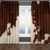A pair of brown and white cow print curtains hanging in a window frame.