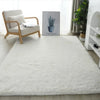 A fluffy white anti-slip floor mat placed on a light wooden floor next to an armchair and a potted plant.