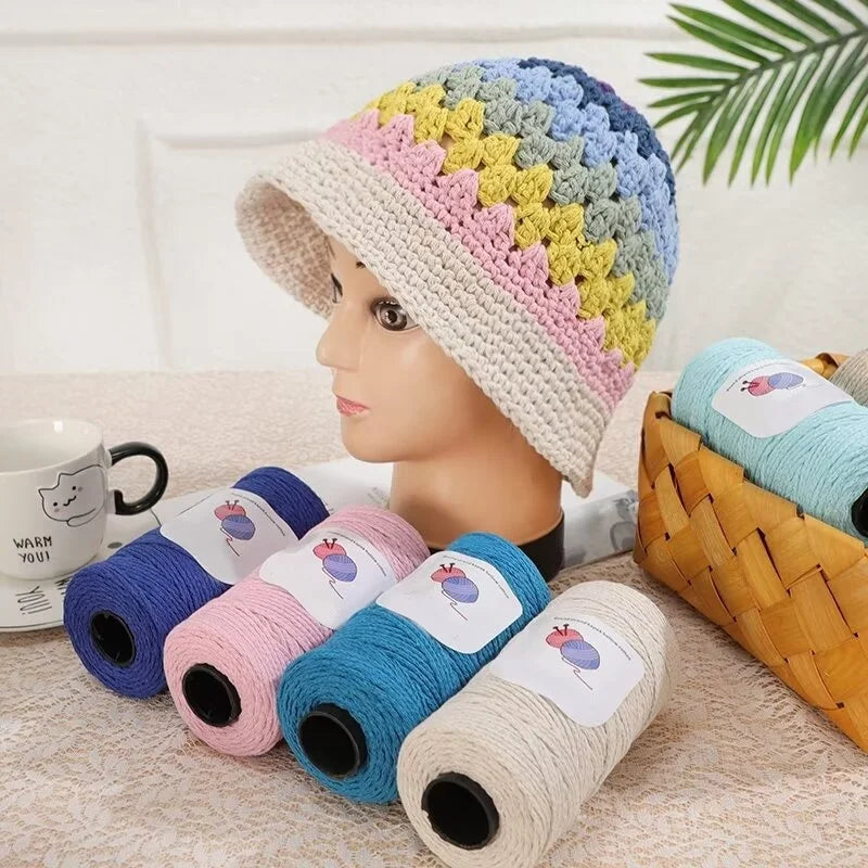 A display of medium-thick hand-woven cotton yarn in a rainbow pattern on a head and several spools.
