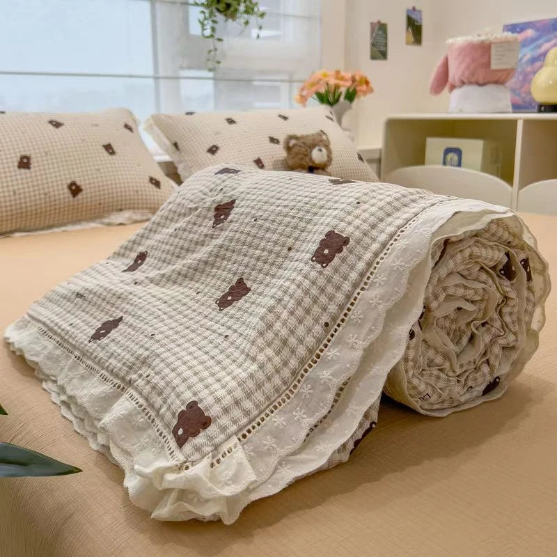 A rolled white quilt blanket with a subtle floral print and decorative lace trim is displayed on a table.