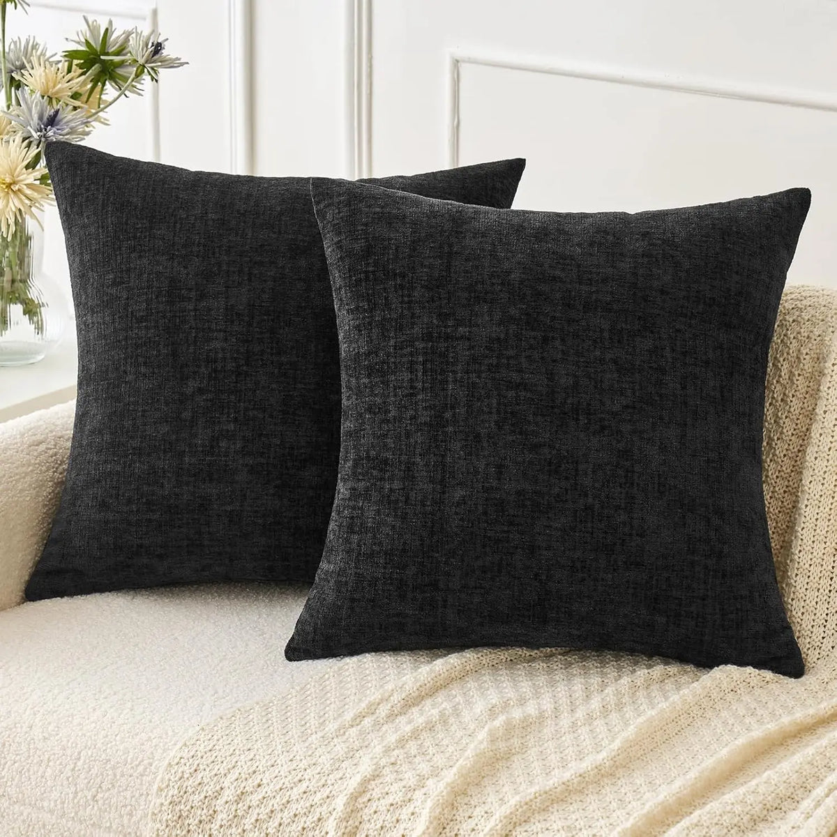 A dark gray chenille throw pillow cover resting on a cream knitted fabric surface.