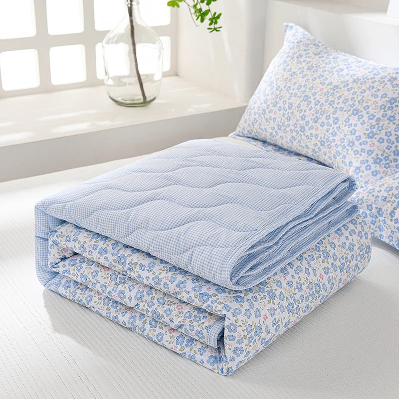 Light blue and white quilted bedding set with a floral pattern displayed on a bed.