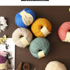 A collection of hand-woven medium thick wool thread in various colors including blue, yellow, beige, and green on a dark wood