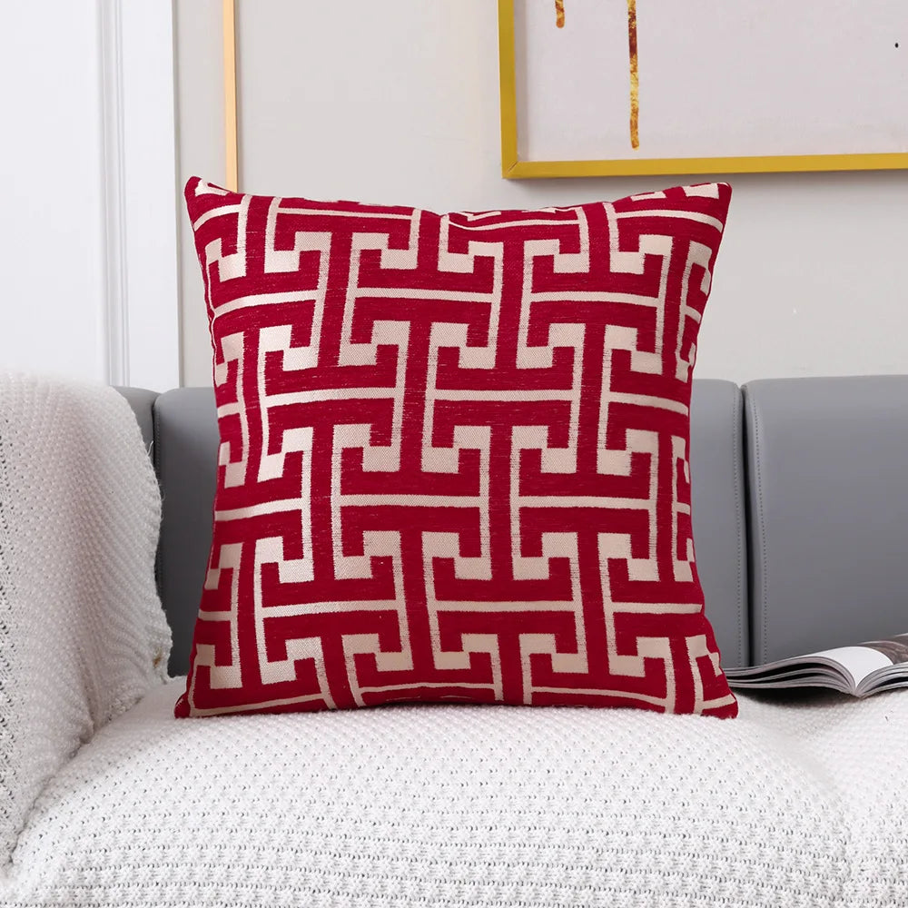 A square red and off-white geometric jacquard lumbar pillow cover resting on a gray sofa.