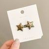 A pair of gold-toned metal star brooch pins displayed on a white card.