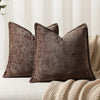 A dark brown chenille throw pillow resting on a cream knitted blanket.