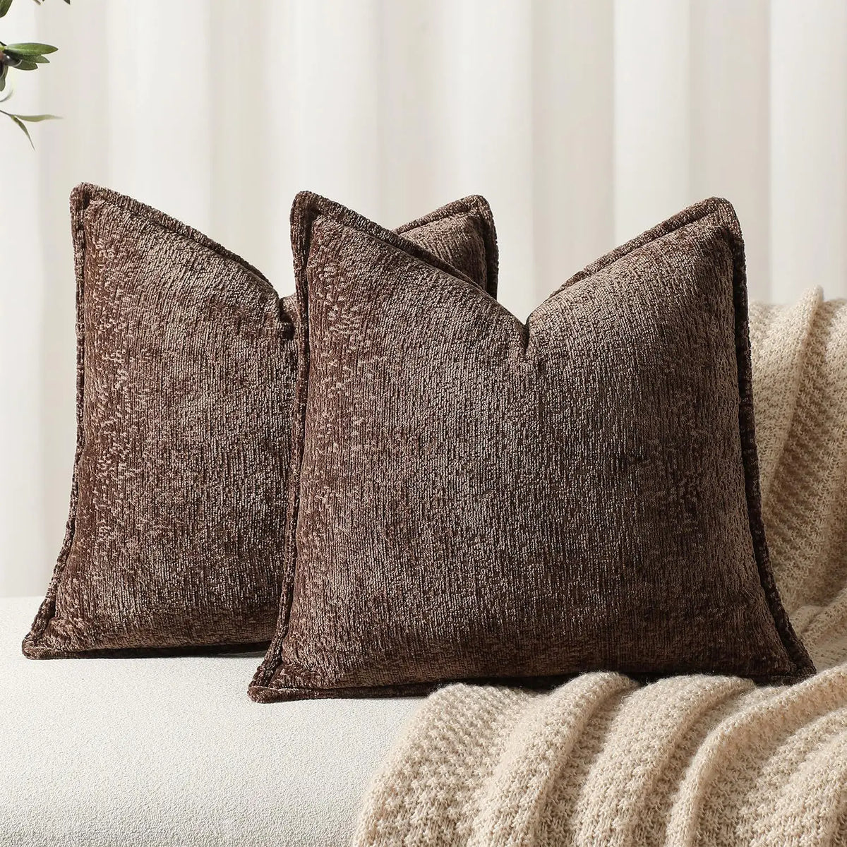 A dark brown chenille throw pillow resting on a cream knitted blanket.