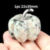 A natural stone pumpkin figurine with a silver stem is held in a person's hand.