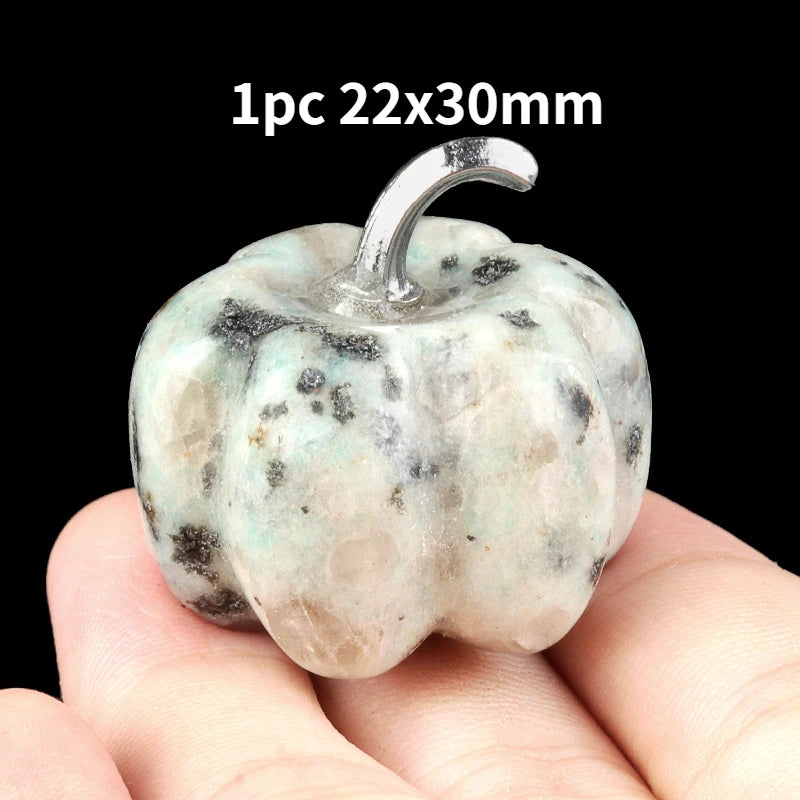 A natural stone pumpkin figurine with a silver stem is held in a person's hand.