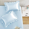 A set of two light blue ruffled satin pillowcases displayed on a light blue surface.