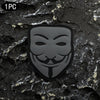 A black embroidered patch featuring a smiling face design with a velcro backing placed on a dark, textured surface.
