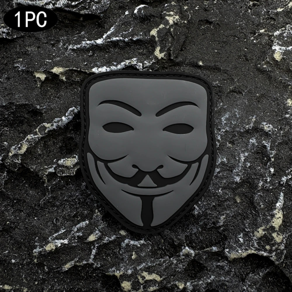 A black embroidered patch featuring a smiling face design with a velcro backing placed on a dark, textured surface.