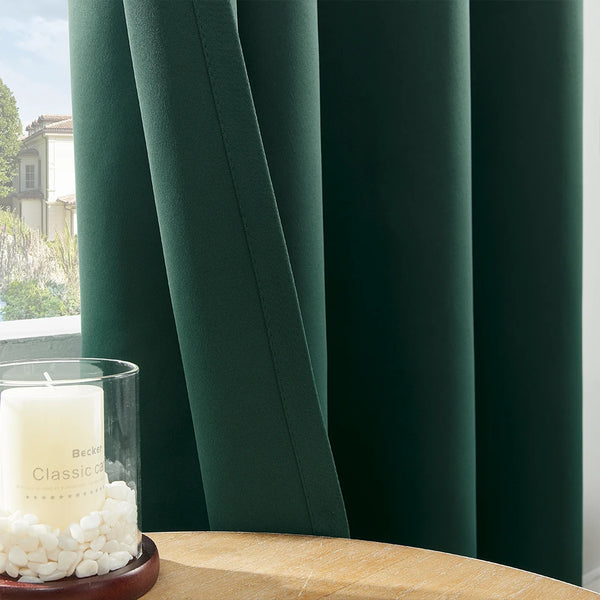 A dark green blackout window curtain is shown next to a glass candle and a wooden surface.