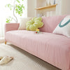 A pink stretchable sofa cover with a vertical line pattern and light green decorative pillows on a beige rug.
