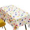 A white disposable plastic tablecloth with colorful polka dots is spread on a table.
