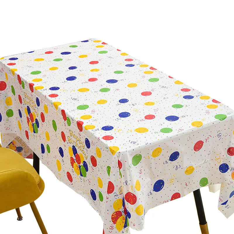 A white disposable plastic tablecloth with colorful polka dots is spread on a table.
