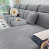 A gray jacquard stretch sofa cover featuring a textured, wavy pattern on a sectional sofa with cream accent pillows.