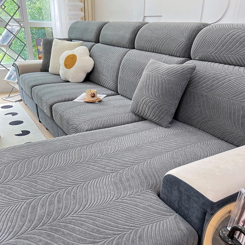 A gray jacquard stretch sofa cover featuring a textured, wavy pattern on a sectional sofa with cream accent pillows.