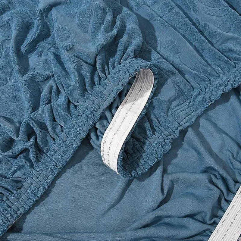 A close-up of a soft blue elastic headboard cover with a white elastic band visible at the opening.