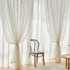 White French country lace curtain with a beaded phoenix tail design hanging in a bright room.