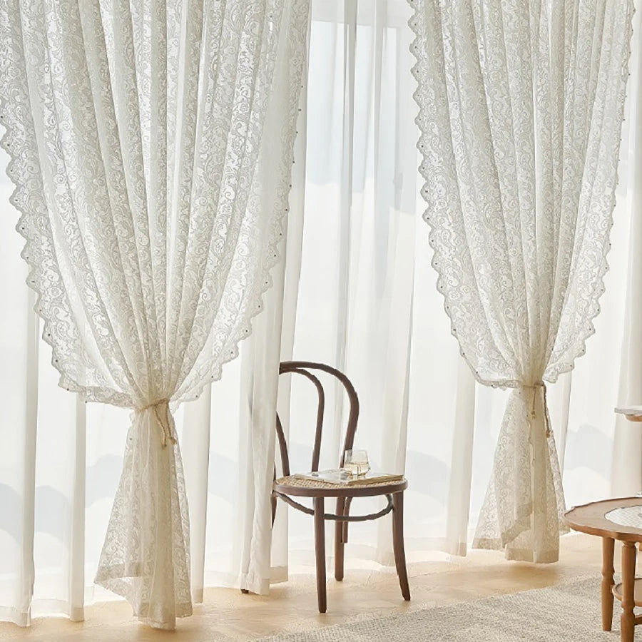 White French country lace curtain with a beaded phoenix tail design hanging in a bright room.