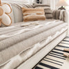 A beige plush velvet sofa protector cover with textured fabric and decorative throw pillows on a light-colored sofa.