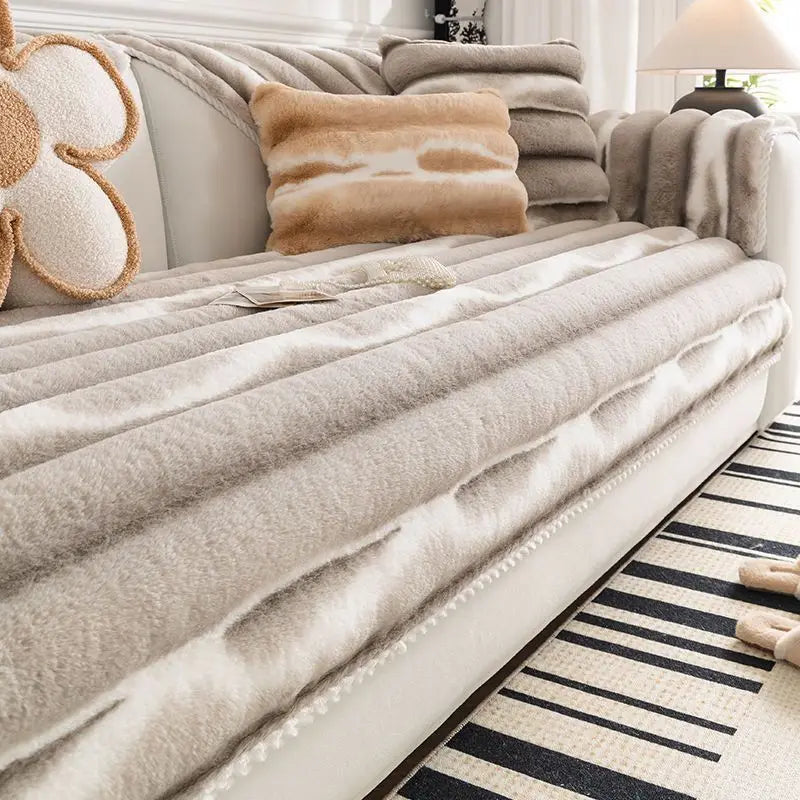 A beige plush velvet sofa protector cover with textured fabric and decorative throw pillows on a light-colored sofa.