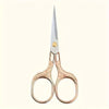 A pair of vintage stainless steel sewing scissors with rose gold handles and a silver blade.