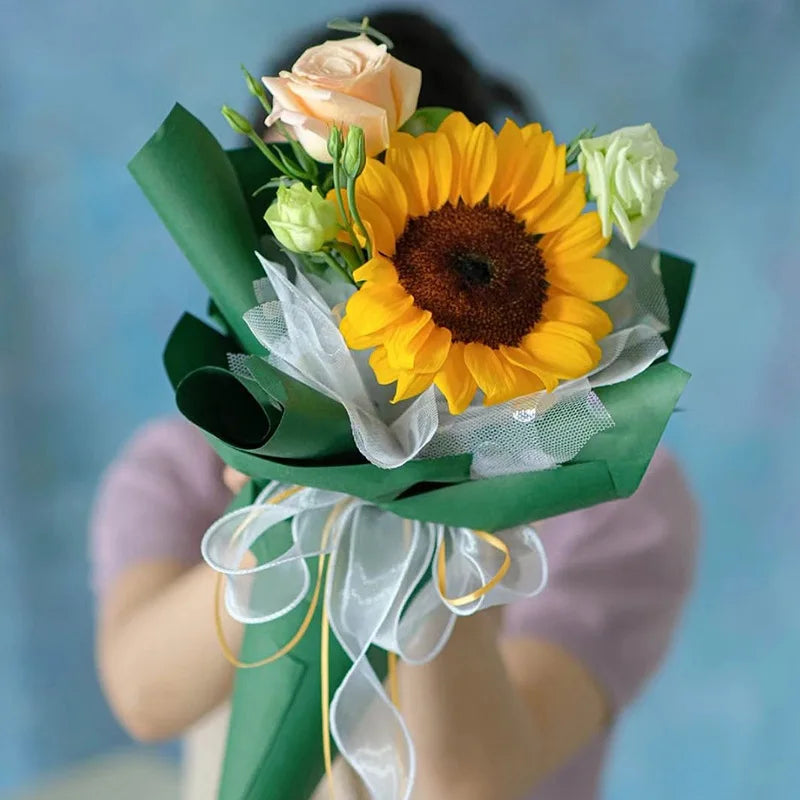 A bouquet of yellow sunflowers and peach roses wrapped in green silky organza ribbon for gift wrapping