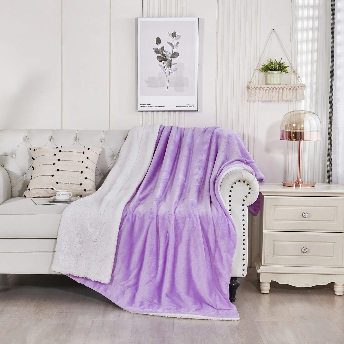 A purple sherpa fleece blanket draped over a white armchair next to a light-colored sofa.