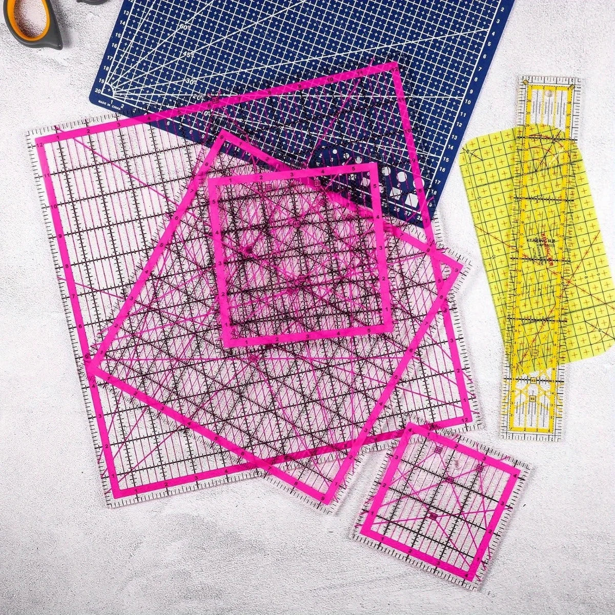 A set of acrylic quilting rulers in various sizes and a ironing ruler laid on a light gray surface.