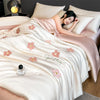 A woman is relaxing under a light pink and cream embroidered quilt in a bedroom setting.