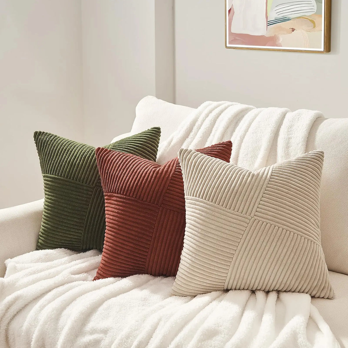 A set of four textured corduroy throw pillow covers in shades of olive green, rust, and beige resting on a white blanket.