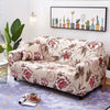 A beige floral patterned universal stretch sofa and chair slipcover displayed on a floor with a framed botanical print.