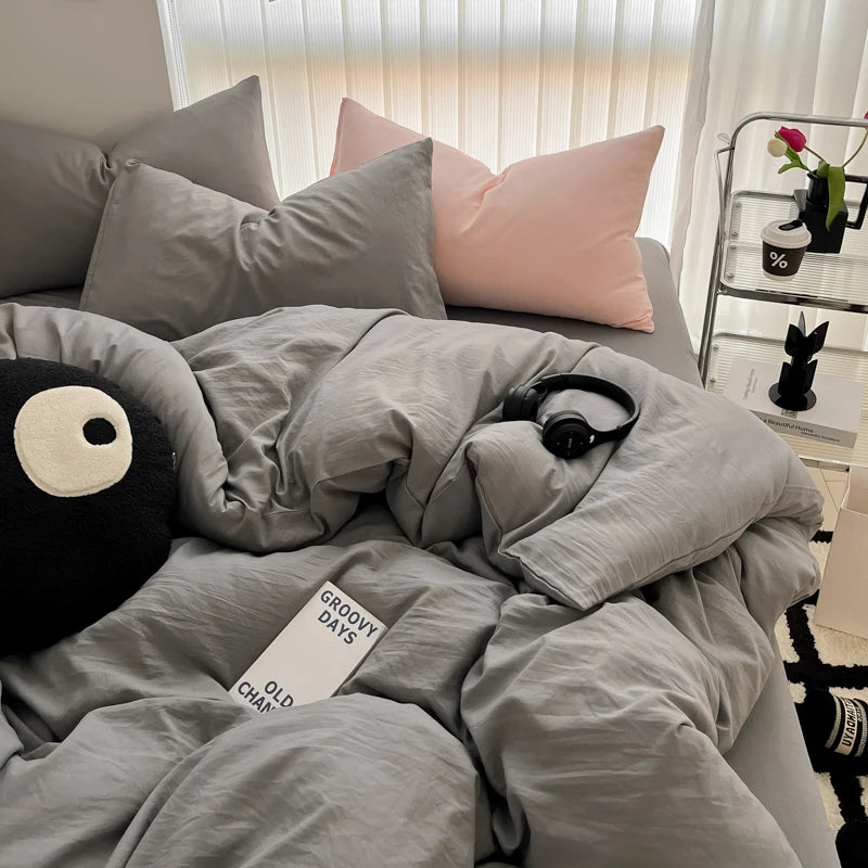 A gray duvet cover set with pillows and a black stuffed animal on a bed.
