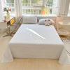 A white organic cotton bedding set featuring a flat sheet, pillowcases, and a small stuffed animal on a bed.