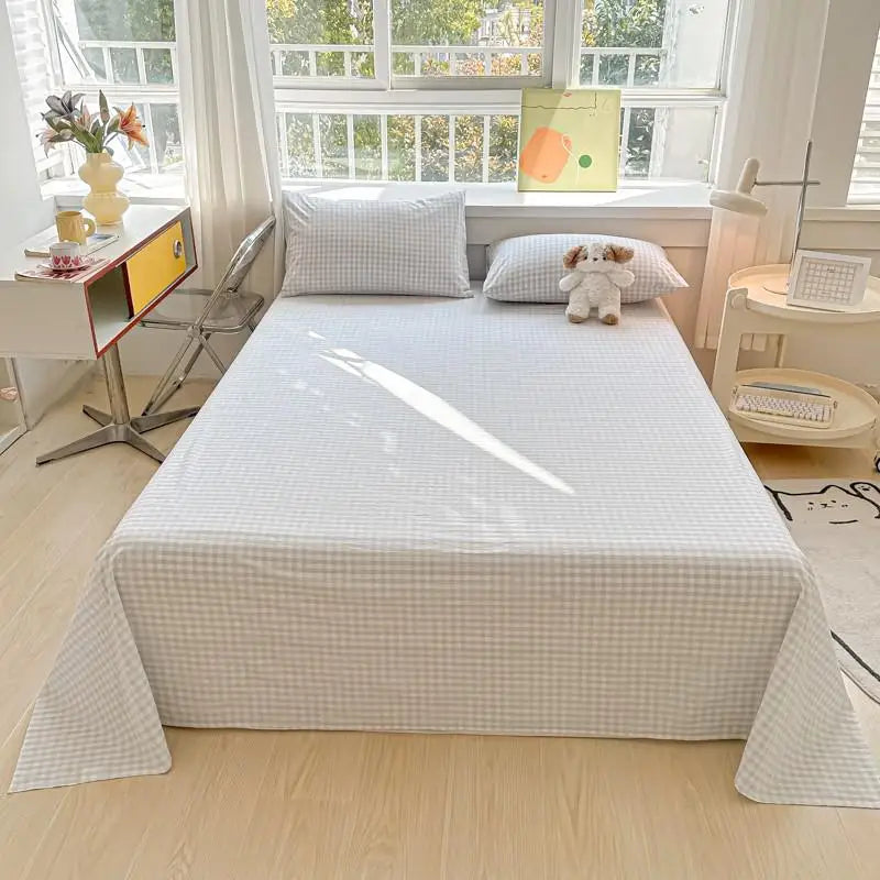 A white organic cotton bedding set featuring a flat sheet, pillowcases, and a small stuffed animal on a bed.