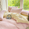 A soft pink and cream checkered duvet cover set with fluffy pillows on a bed near a large window.