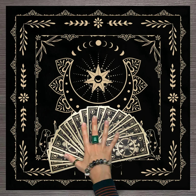 A hand holds a fan of tarot cards within a decorative mat featuring floral and celestial designs.