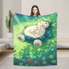A person holds up a plush decorative throw blanket featuring a sleeping green creature surrounded by green grass and small fl