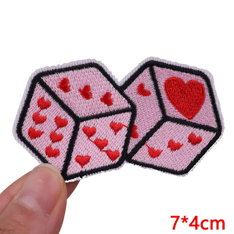 Two pink dice with red heart embroidery shown being held, measuring 7x4cm.