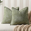 A close-up of a moss green chenille throw pillow resting on a beige textured fabric.