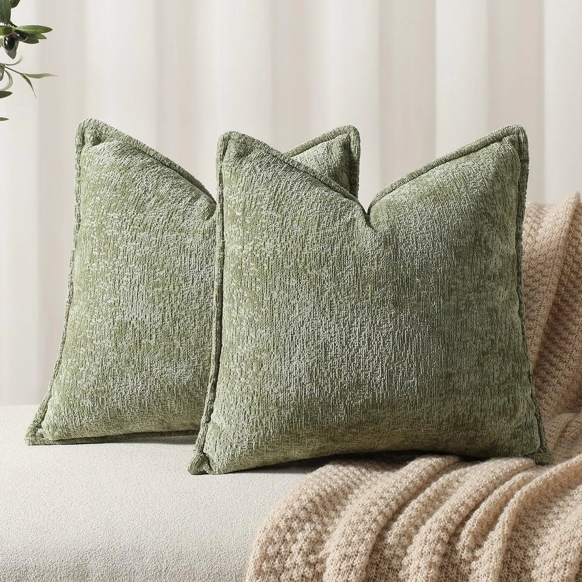 A close-up of a moss green chenille throw pillow resting on a beige textured fabric.