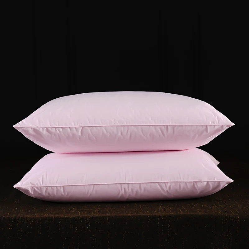 Two pink natural goose down and feather sleeping pillows resting on a dark surface.