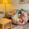 A large, colorful inflatable storage bag filled with various plush toys sits on a rug next to a wooden table.