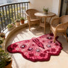 A vibrant pink and maroon irregular shaped plush floor rug is displayed in a bright indoor setting with wicker furniture.