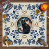 A floral tarot card mat featuring a silhouette of a black cat against a moonlit background.