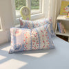 A light blue duvet cover set with patterned pillowcases and a yellow alarm clock on a white bed.